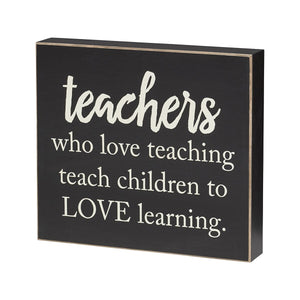 Wooden box sign painted black with white lettering that reads "Teachers Who Love Teaching Teach Children To Love Learning".